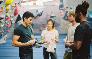 Smart Start: Essential Bouldering Gear Guide Four diverse climbers in a bouldering gym examining new bouldering gear, including shoes and a chalk bag, representing an essential bouldering gear guide.