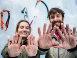 Close-up of two ice climbing gloves on hands, one thin and one thick, against a blurred ice climbing background, demonstrating a multi-glove system for ice climbing.