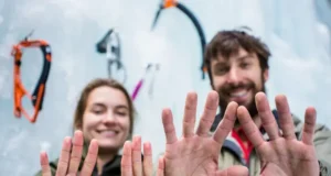Beyond One Pair: The Ultimate Ice Climbing Glove System Close-up of two ice climbing gloves on hands, one thin and one thick, against a blurred ice climbing background, demonstrating a multi-glove system for ice climbing.
