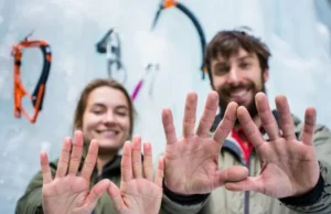 Beyond One Pair: The Ultimate Ice Climbing Glove System Close-up of two ice climbing gloves on hands, one thin and one thick, against a blurred ice climbing background, demonstrating a multi-glove system for ice climbing.