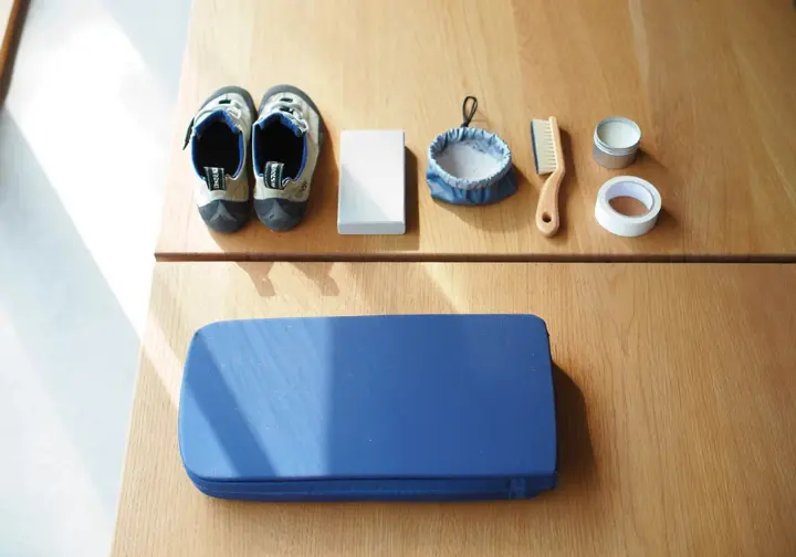 A tiered display of bouldering gear, showing climbing shoes, chalk, a chalk bag in the foreground, a crash pad in the middle, and a brush, tape, and skin balm in the background, illustrating a bouldering gear hierarchy for beginners.