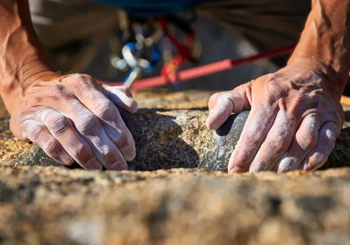 Hands of a climber on natural rock, illustrating the definition and spectrum of style and purity in first ascent rock climbing.
