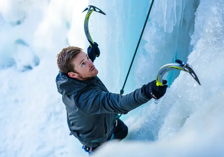 An ice climber gripping ice tools on a frozen waterfall, illustrating the struggle against cold and the physical demands of ice climbing.