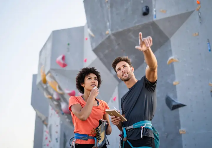 Two diverse climbers discuss the experience at the base of a huge artificial climbing wall, evaluating if the climb lives up to the hype for the largest climbing walls.