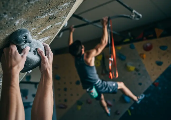 A close-up of hands gripping a rock hold, with a pull-up in the background, illustrating the core components of a balanced rock climbing training program.