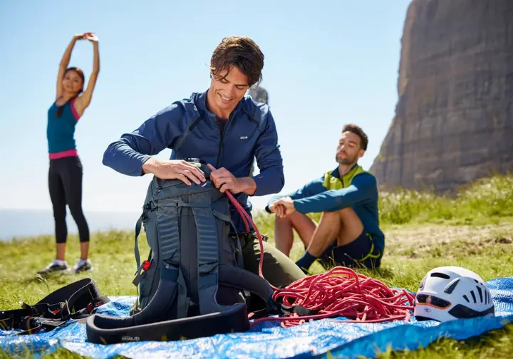 A climber packing gear, another stretching, and a third sitting calmly, representing the packing, training, and mental readiness for an outdoor rock climbing camp.