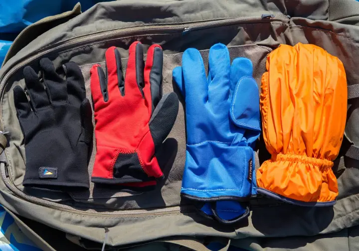 An organized flat lay of a complete ice climbing glove system, showing a liner, lead glove, belay mitt, and emergency mitt.