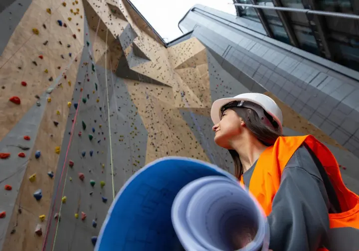 A striking architectural climbing wall integrated into a modern building, with an engineer observing, representing the vision and engineering of the world's largest climbing walls.