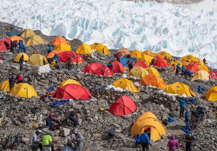 A wide shot of Everest Base Camp with climbers and tents, showing the strategic activity of acclimatization with the Khumbu Icefall visible in the distance.