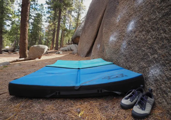 A bouldering crash pad laid out beneath a rock formation outdoors, symbolizing the essential safety equipment for outdoor bouldering gear.