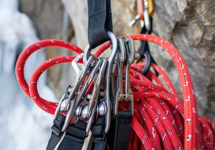 A detailed view of an organized ice climbing rack with ice screws and quickdraws, and a dry-treated climbing rope, representing the logistics and protection system.