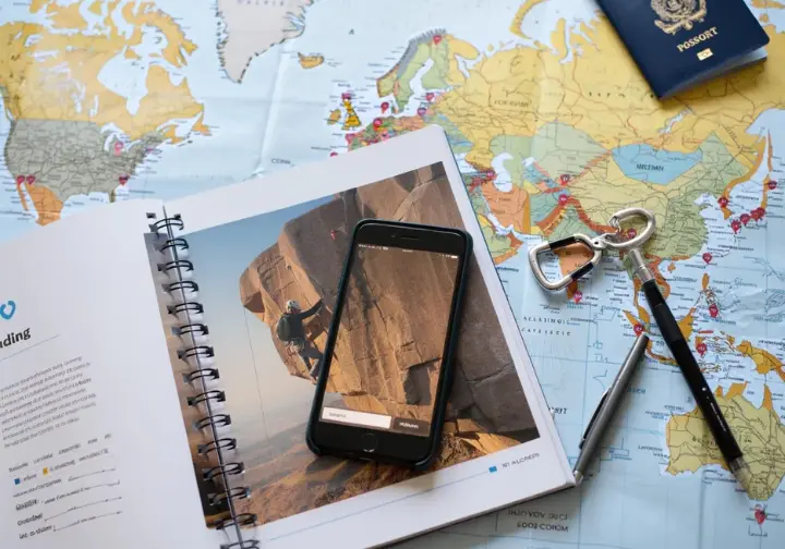 Flat lay showing a world map with a passport, guidebook, and climbing gear, representing a traveling climber planning an ascent of the largest climbing walls worldwide.