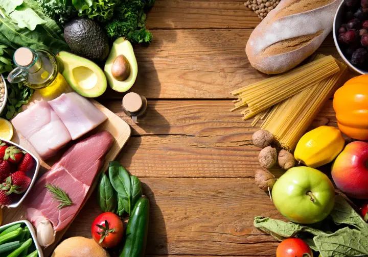 An overhead shot of a wooden table with healthy ketogenic foods on one side and foods to avoid on the other, illustrating how to build a ketogenic meal plan.