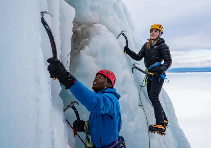 Ice climbers navigate a hazardous icy cliff face with falling ice in Michigan's U.P., emphasizing safety in ice climbing.