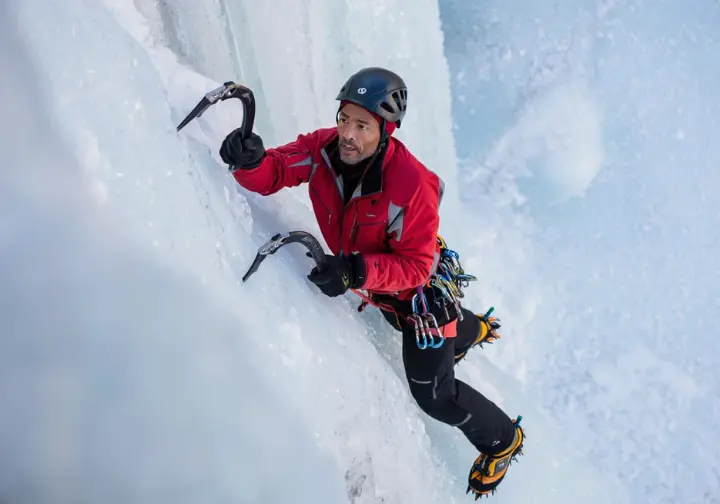 An experienced ice climber demonstrating precise and controlled movement while placing an ice screw on a steep ice wall, embodying the "don't fall" mindset.