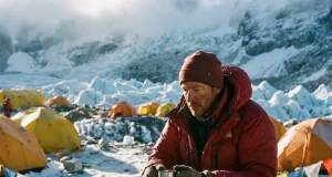 Why a Trip to Climb Mount Everest Is 90% Waiting Climber in a red down suit resting at Everest Base Camp below the Khumbu Icefall at dawn
