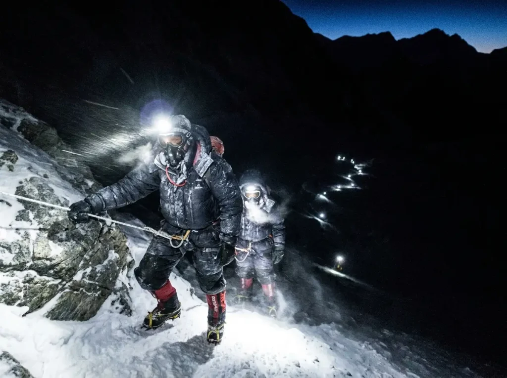 Climbers ascending a fixed rope by headlamp in the dark during the Everest summit push