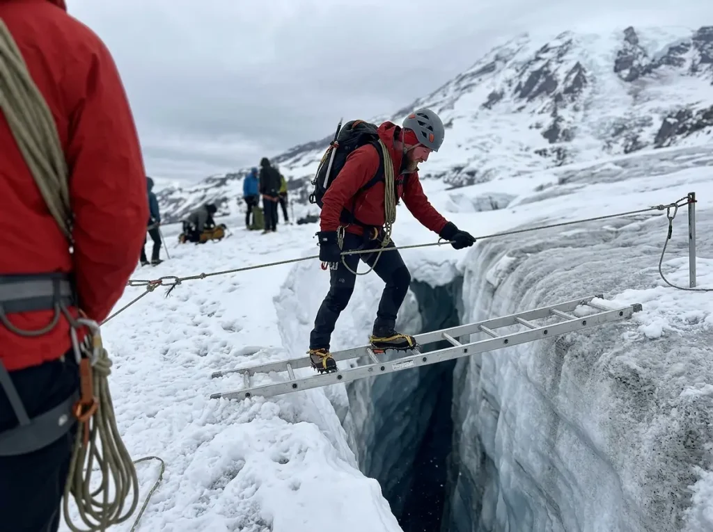 A roped mountaineer crosses an aluminum ladder over an open crevasse on Mount Rainier, clipped to a fixed handline.
