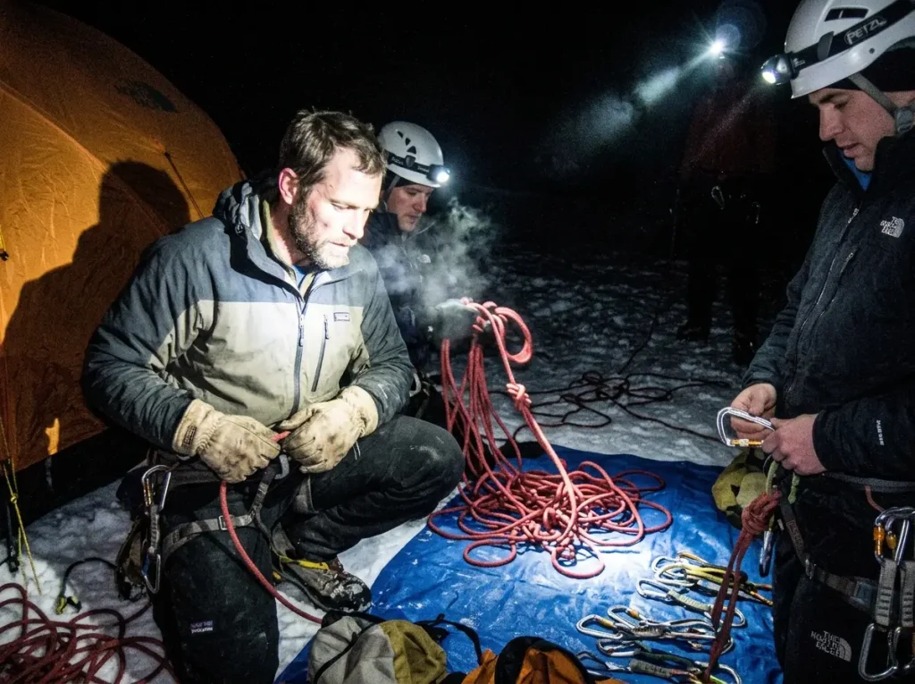 A rope team checks harnesses, rope, and carabiners by flash in the pre-dawn dark at a high camp on Mount Rainier.