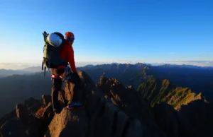 Summit Ready: 7 Beginner Peaks & How to Climb Them A beginner climber stands on a mountain summit at sunrise, looking out at a vast mountain range, ready for the next challenge.