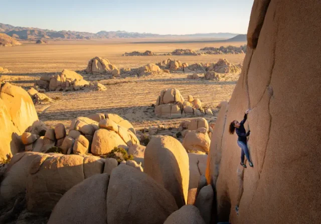 A climber on a massive granite boulder in a stunning valley, representing the best bouldering in the world for all levels.