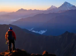 A climber overlooks a vast mountain range at sunrise, with accessible trekking peaks in the foreground and towering technical summits like Denali or Everest in the distance.