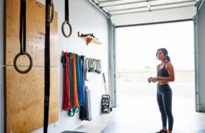Choosing Climbing Training Tools: An Expert Guide A female climber stands in her bright home gym, thoughtfully choosing from a selection of rock climbing training tools including a hangboard and gymnastics rings.