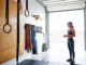 Choosing Climbing Training Tools: An Expert Guide A female climber stands in her bright home gym, thoughtfully choosing from a selection of rock climbing training tools including a hangboard and gymnastics rings.