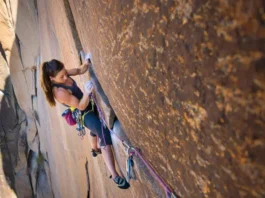 A focused female climber inspects her chalky hand while clinging to a granite rock face, illustrating the science of climbing injuries and prevention.