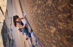 The Science of Climbing Injuries: Prevention & Treatment A focused female climber inspects her chalky hand while clinging to a granite rock face, illustrating the science of climbing injuries and prevention.