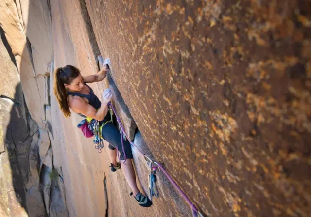 A focused female climber inspects her chalky hand while clinging to a granite rock face, illustrating the science of climbing injuries and prevention.