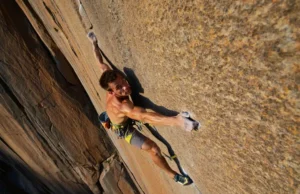FRC Explained: Injury-Proof Your Hips & Shoulders A rock climber demonstrates injury-proof hip and shoulder mobility with a confident high-step and wide reach on a sunny outdoor rock face.