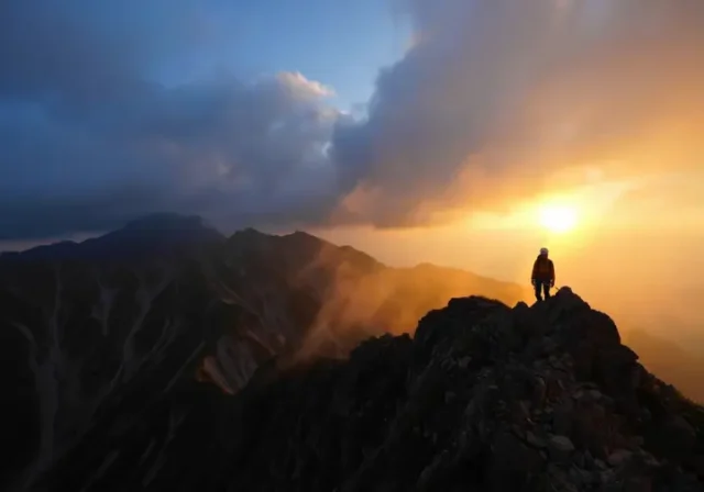 A climber stands on a high mountain ridge, observing a dramatic sky split between golden sunlight and approaching storm clouds, illustrating the volatility of mountain meteorology.