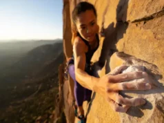 Climber’s Anatomy 101: Your Guide to Injury-Free Hands A skilled female climber's strong, chalked hands gripping a granite rock face during sunrise, illustrating the theme of a guide to injury-free hands in climbing.