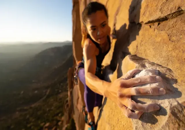 A skilled female climber's strong, chalked hands gripping a granite rock face during sunrise, illustrating the theme of a guide to injury-free hands in climbing.