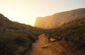 Do You Need Both Hiking and Climbing Shoes? The Answer A scenic hiking trail winds through a mountain valley, leading directly to the base of a large granite climbing cliff at sunset.
