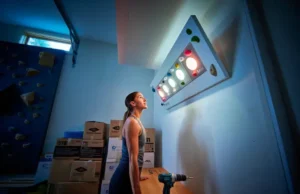 Kilter vs. Moonboard vs. Tension: A Cost & Training Test A female climber stands in her modern garage gym, thoughtfully looking up at her new LED training board, representing the choice between Kilter, Moonboard, or Tension.