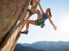Mobility for Climbers: Unlock High-Steps & Heel-Hooks A female climber demonstrates an advanced mobility move, performing a high-step on a sunny outdoor rock wall, showcasing flexibility and strength.