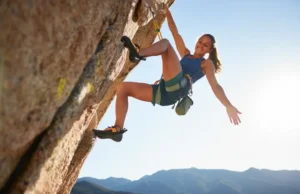 Mobility for Climbers: Unlock High-Steps & Heel-Hooks A female climber demonstrates an advanced mobility move, performing a high-step on a sunny outdoor rock wall, showcasing flexibility and strength.