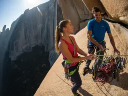 Two competent climbers at a sunny belay station on a vast granite cliff, organizing their gear and ropes as they prepare for the next pitch of their multi-pitch climb.