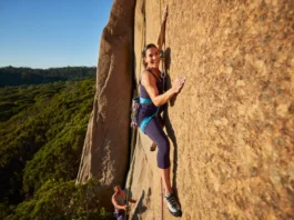 An empowered pregnant woman rock climbing safely outdoors while wearing a full-body harness, representing the journey of rock climbing and pregnancy.