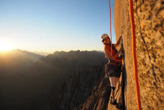 Essential Types of Rope Climbing: Top-Rope, Lead & More A female climber with a prosthetic leg rock climbing on a large cliff, representing the essential types of rope climbing.