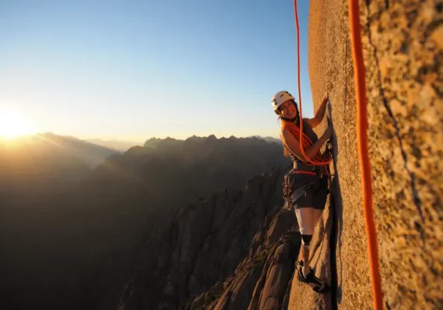 00 types-of-rope-climbing-hero-image A female climber with a prosthetic leg rock climbing on a large cliff, representing the essential types of rope climbing.