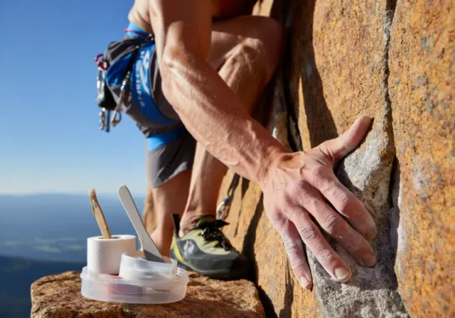 A rock climber confidently gripping a rock face with healthy hands, alongside a subtle climbing skin care kit on a nearby ledge, symbolizing preparedness and optimal hand health.