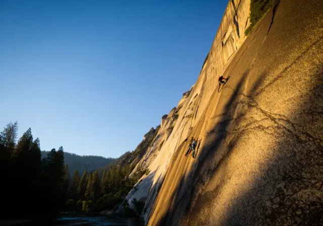 Two climbers ascend the massive granite face of El Capitan during golden hour, representing the challenge of rock climbing in Yosemite National Park.