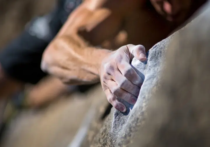 A close-up view of a climber's hand under immense strain on a small crimp hold, demonstrating the fundamental science behind climbing injuries.
