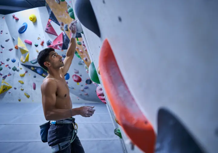A male climber thoughtfully studying a bouldering wall, representing the foundational principles of a climbing workout.
