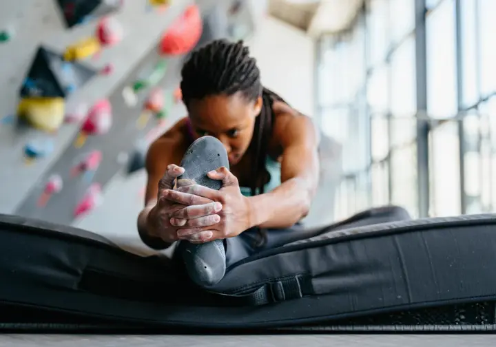 A climber in a gym demonstrates the difference between passive flexibility and active mobility during a targeted hip stretch.