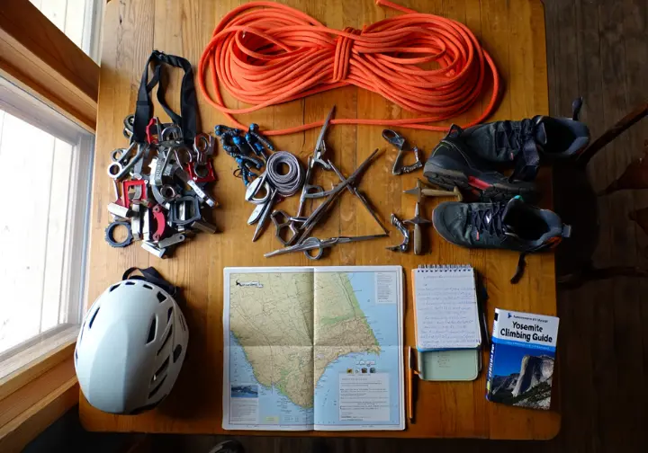 A flat lay of climbing gear for a Yosemite trip, including a rope, trad rack, helmet, and planning guidebook, symbolizing logistics and preparation.