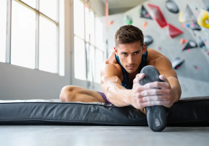 A climber performs a controlled mobility exercise in a brightly lit gym, illustrating the science of movement for climbing performance.